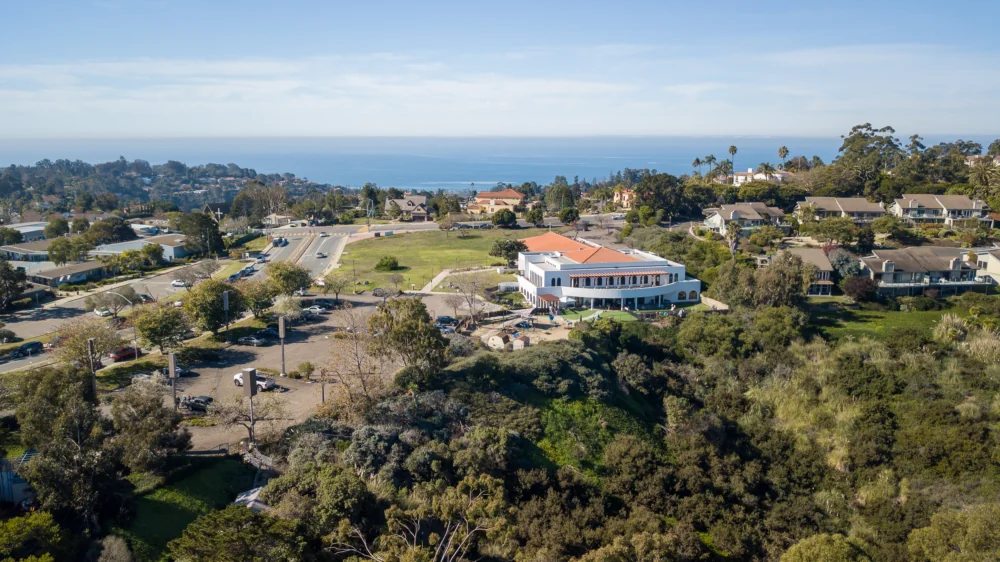 Drone image of white education building with trees and ocean in the background